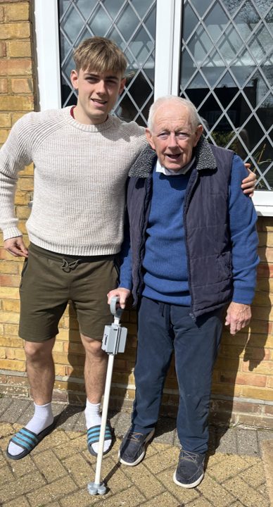Euan standing beside his grandad, who is smiling and holding the Smart Walking Stick prototype in his hand